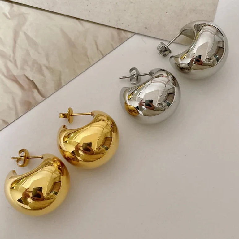 Gold and silver earrings on a light surface with a mirror reflection.