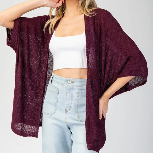Woman wearing a burgundy cardigan over a white top and light blue jeans on a plain background