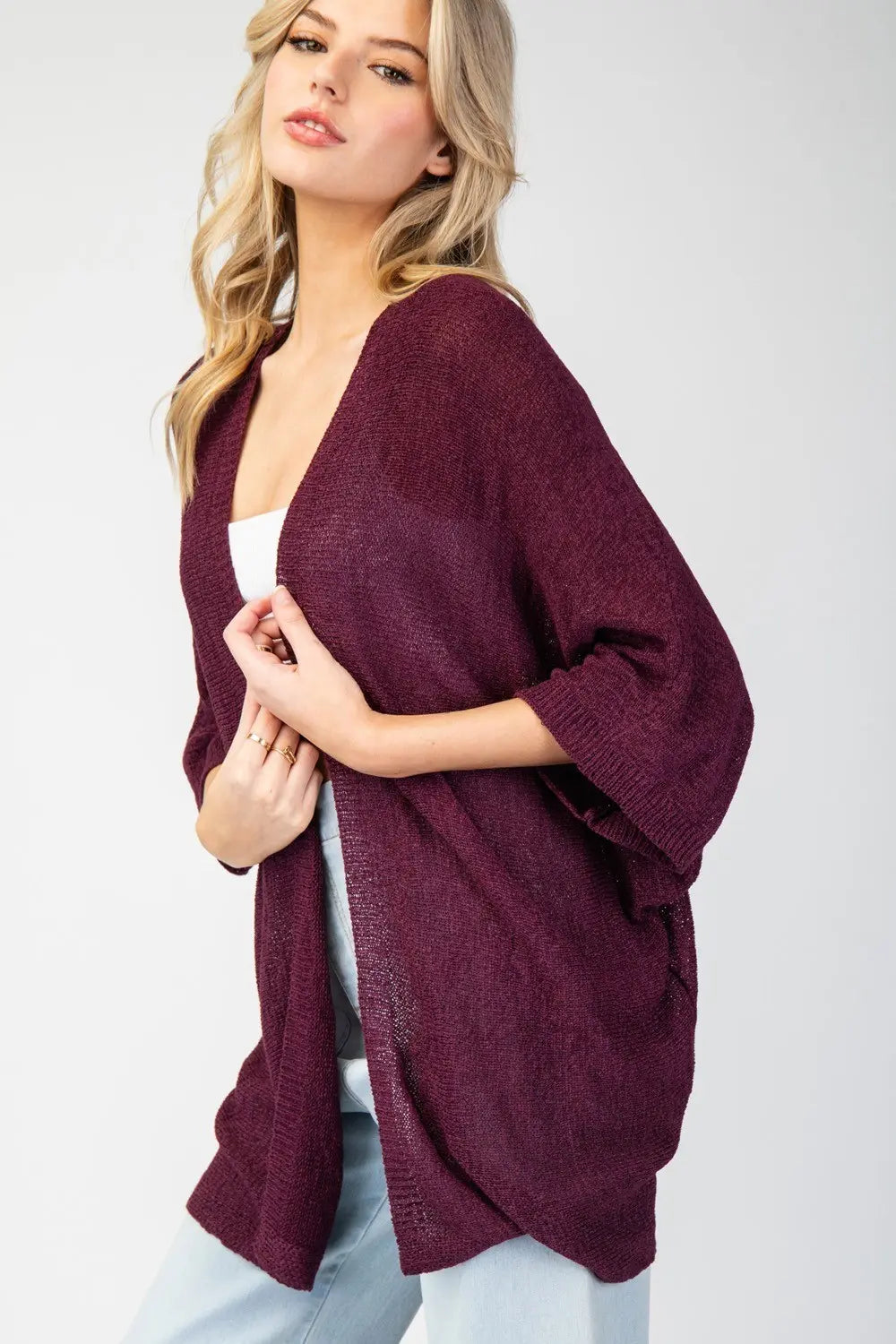 Woman wearing a burgundy cardigan over a white top on a plain background