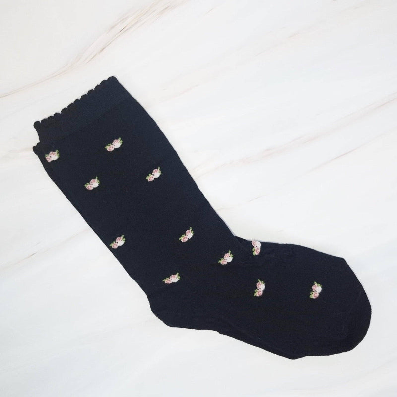 Black sock with small white floral patterns on a light wooden floor.