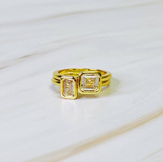 Gold ring with emerald-cut gemstones on a light marble background
