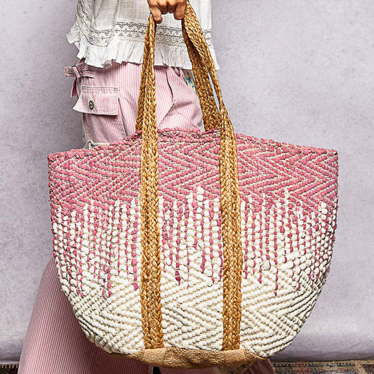 Person holding a pink and white woven bag with natural handle