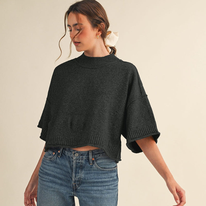 Woman wearing a dark gray sweater and blue jeans on a beige background