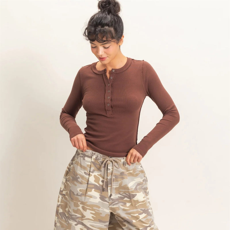 A woman modeling a brown long-sleeve henley top and beige camouflage drawstring shorts against a plain light background.