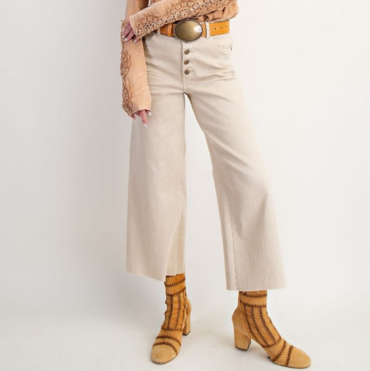Woman wearing a beige shirt, white pants, and a straw hat on a white background