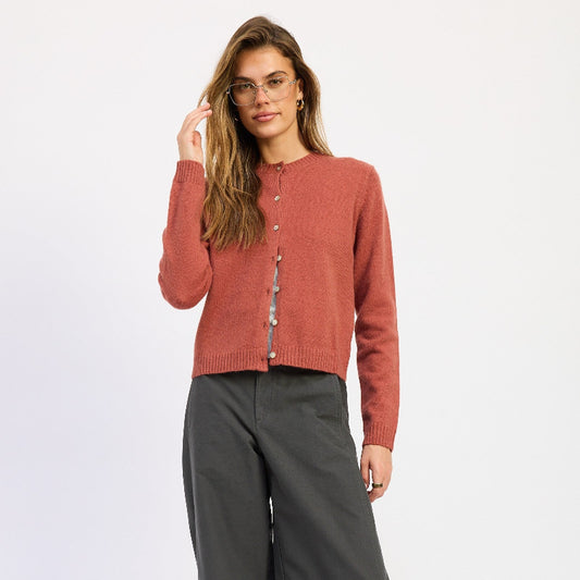 A woman modeling a terracotta-colored knit cardigan with buttons, paired with dark gray wide-leg trousers and brown shoes, against a plain white studio background.