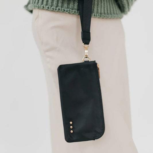 Black crossbody bag with gold accents held by a person wearing beige pants and a green sweater.