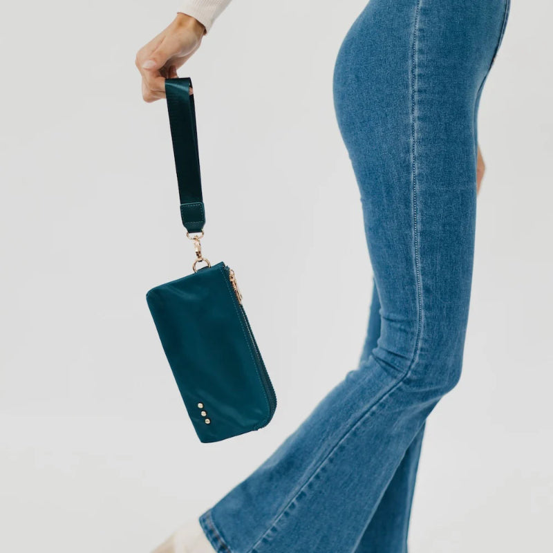Teal handbag held by a person wearing blue jeans on a light gray background