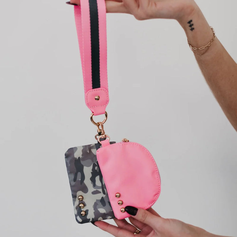 Pink and camouflage pouches with a strap held by a hand against a plain background