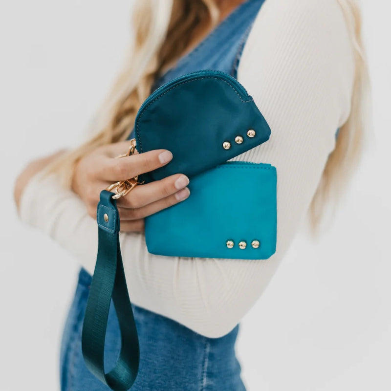 Teal clutch with gold accents held by a person wearing a white sweater and blue jeans.