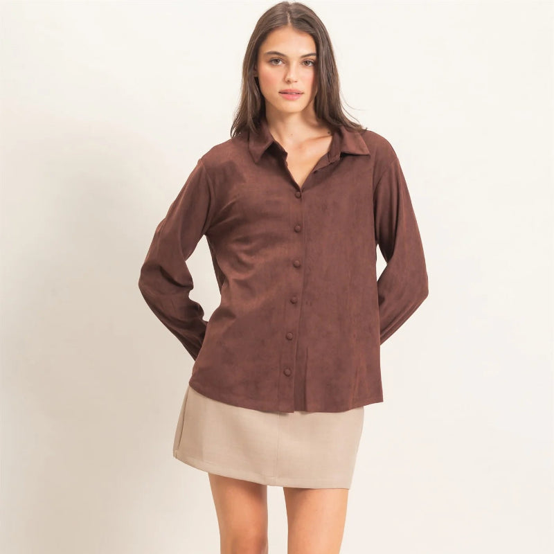 A woman modeling a brown long-sleeve button-up shirt with a beige mini skirt and black strappy sandals, standing against a plain light background.