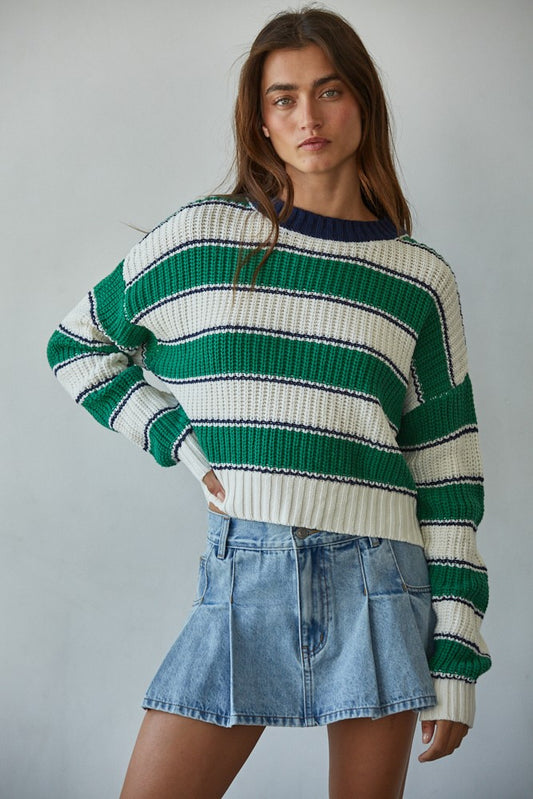 Woman wearing a green and white striped sweater with a denim skirt on a gray background