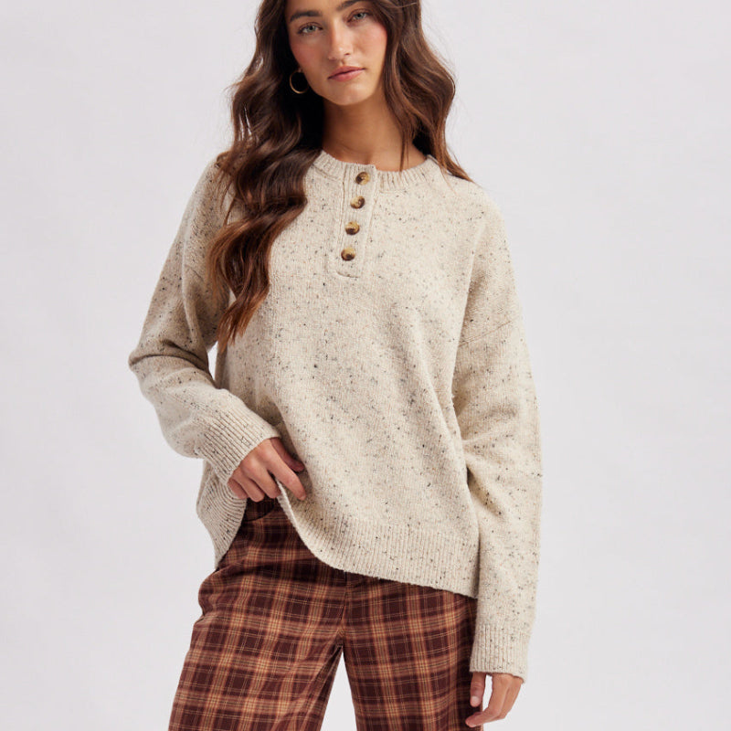 A woman modeling a cozy knit long-sleeve henley top in cream and rust plaid wide-leg pants, paired with tan suede mules, against a light gray studio background.
