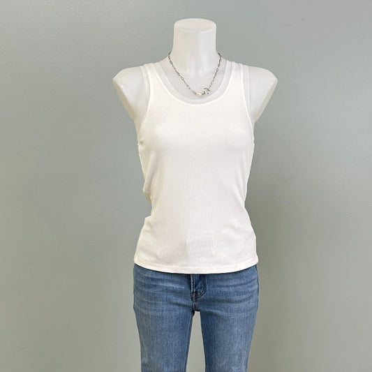 Mannequin wearing a white tank top and blue jeans against a gray wall.