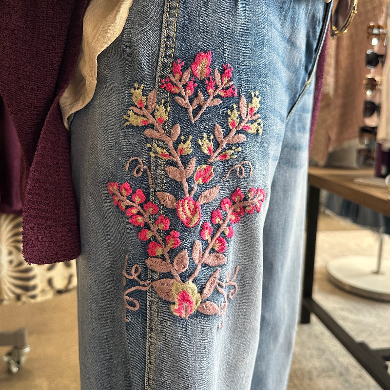 Close-up of blue jeans with floral embroidery on a clothing rack.