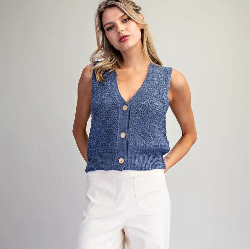 Woman wearing a blue sleeveless top and white pants on a gray background