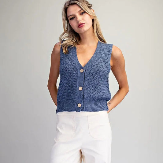 Woman wearing a blue sleeveless top and white pants on a gray background