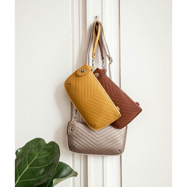 Three quilted handbags in yellow, brown, and beige hanging on a white door.
