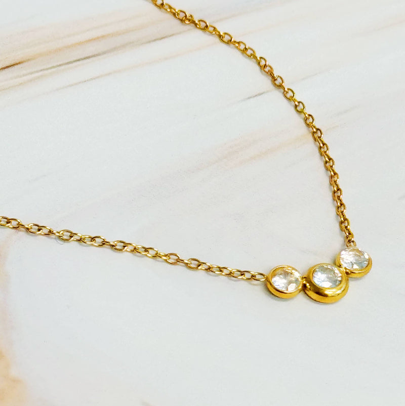 Gold necklace with three clear gemstones on a light background