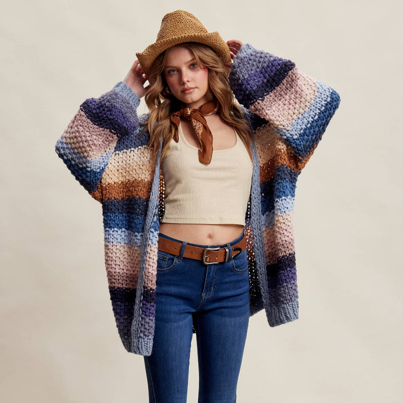 Woman wearing a colorful cardigan, blue jeans, and brown boots with a neutral background