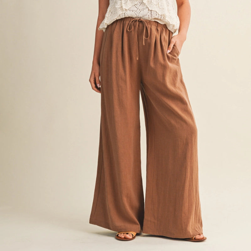 Woman wearing a white lace top and brown wide-leg pants on a beige background