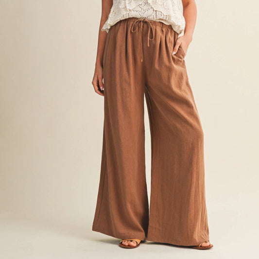 Woman wearing a white lace top and brown wide-leg pants on a beige background