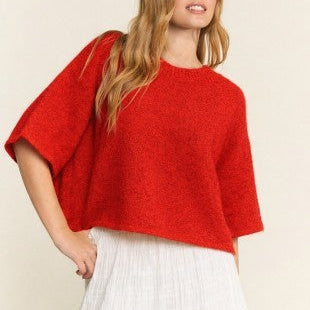 Woman wearing a red sweater and white pants against a beige background