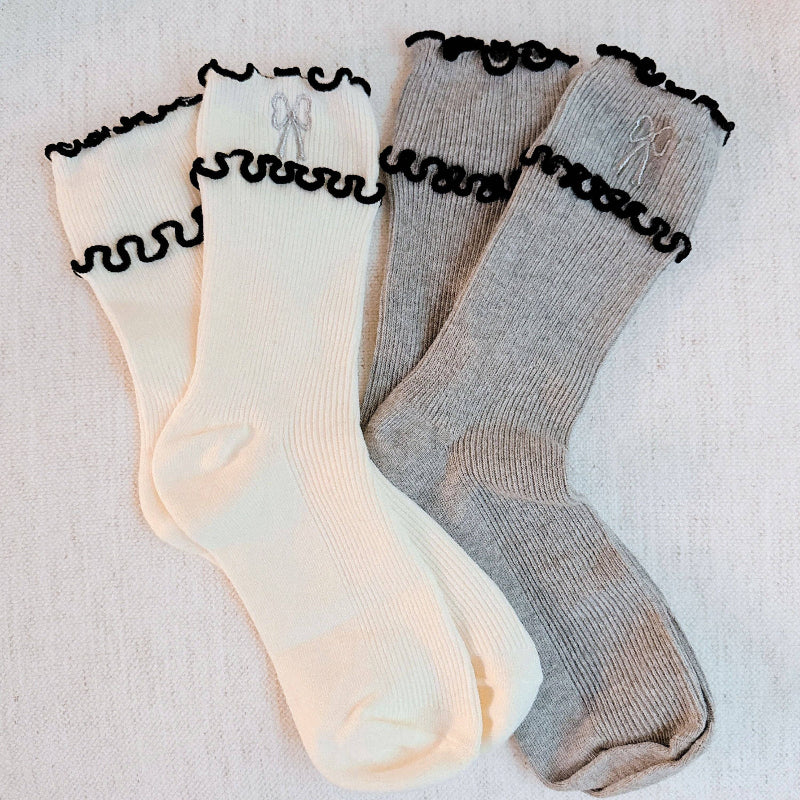 Two pairs of socks, one beige and one gray, with decorative black trim on a light background.