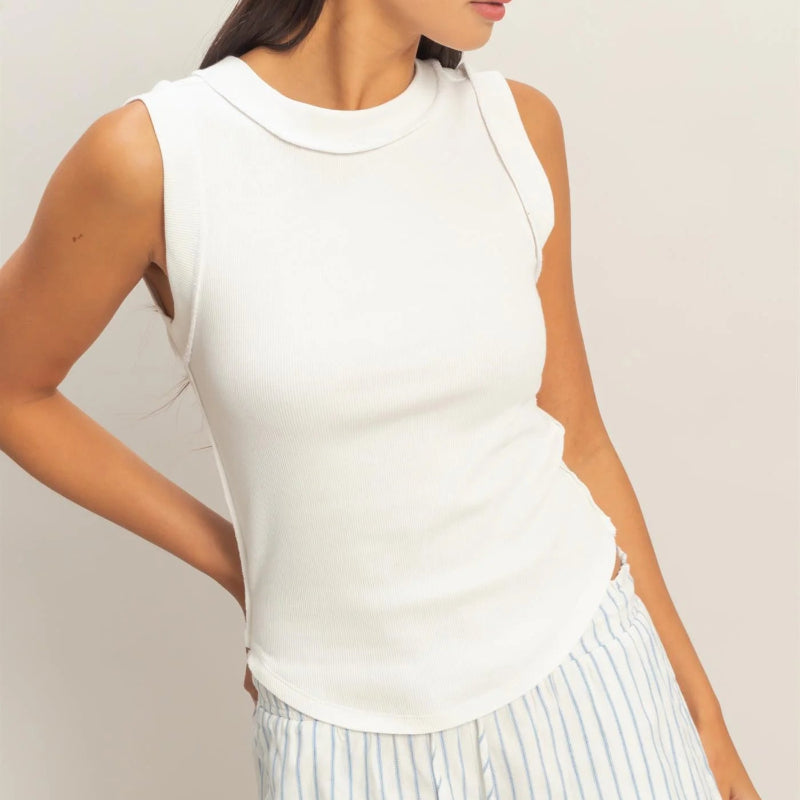 Woman wearing a white sleeveless top and striped pants against a plain background