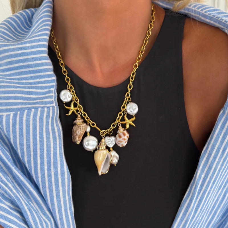 Necklace with shell and pearl charms worn by a person in a blue and white striped shirt.