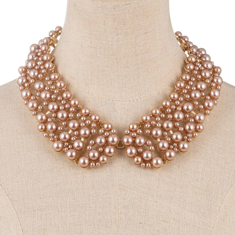 A multi-strand pearl collar necklace in a champagne pink tone with gold-toned metal, displayed on a beige linen dress form against a white background.
