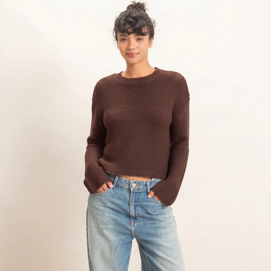 A woman modeling a brown ribbed knit long-sleeve sweater and light-wash wide-leg jeans against a plain off-white studio background.