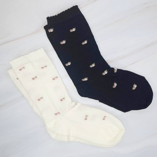 Two pairs of socks, one navy and one white, with small decorative elements on a light wooden surface.