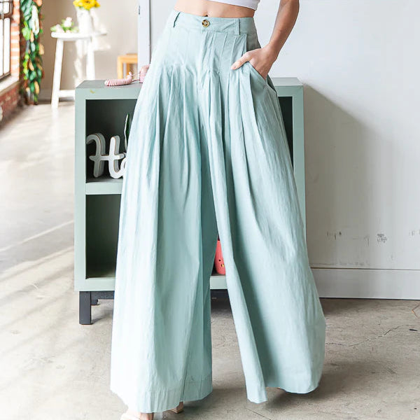 Woman wearing a white crop top and light green wide-leg pants in a bright room.