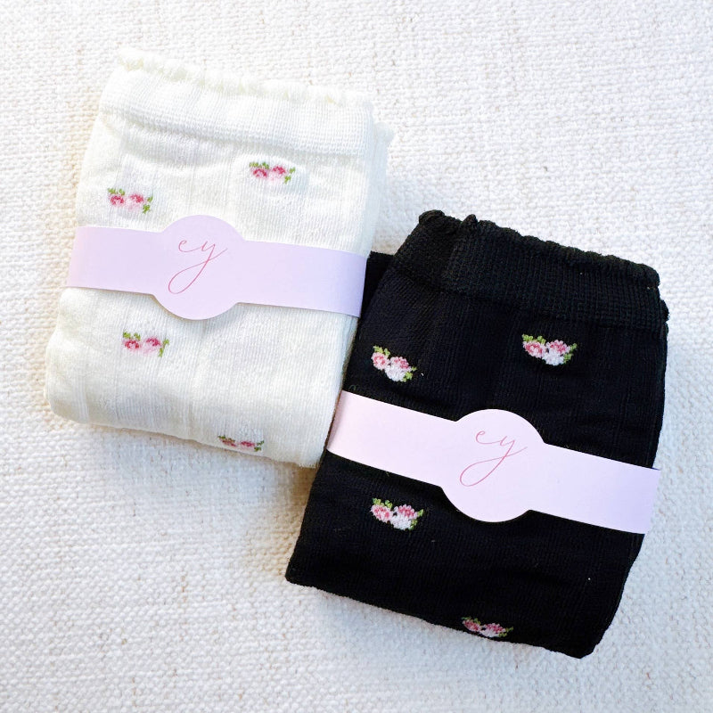 Two pairs of socks, one white and one black, with floral designs and pink bands on a textured surface.