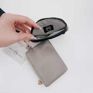 Hand holding a small black and white patterned pouch over a gray wallet on a white background